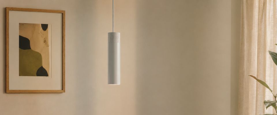 En vit f&ouml;nsterlampa h&auml;nger framf&ouml;r beige v&auml;gg n&auml;ra gardin, tavla och gr&ouml;n v&auml;xt, d&auml;r den ger mjukt riktat ljus. Elbutik.se erbjuder belysning f&ouml;r stilrena f&ouml;nster- och hemmilj&ouml;er.