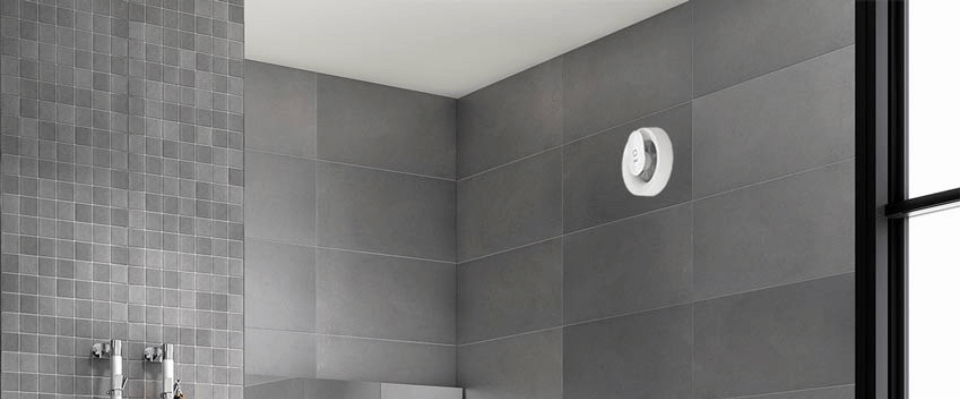 En vit PAX badrumsfl&auml;kt &auml;r installerad p&aring; en m&ouml;rk kaklad badrumsv&auml;gg och ventilerar utrymmet f&ouml;r att minska fukt och f&ouml;rb&auml;ttra inomhusklimatet. Denna ventilationsl&ouml;sning finns hos Elbutik.se och har en stilren, kompakt design.